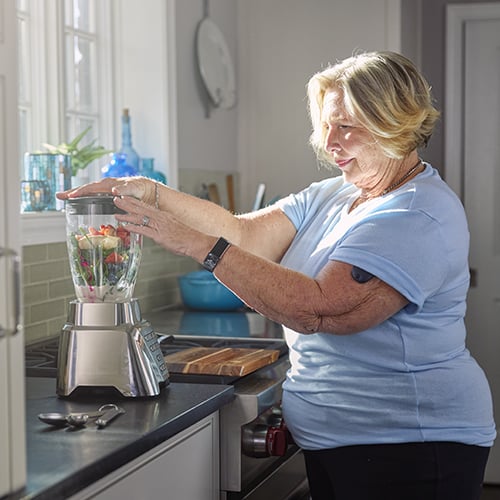 Kobieta przygotowująca w domu koktajl, która ma założony bezprzewodowy system do monitorowania stężenia glukozy.